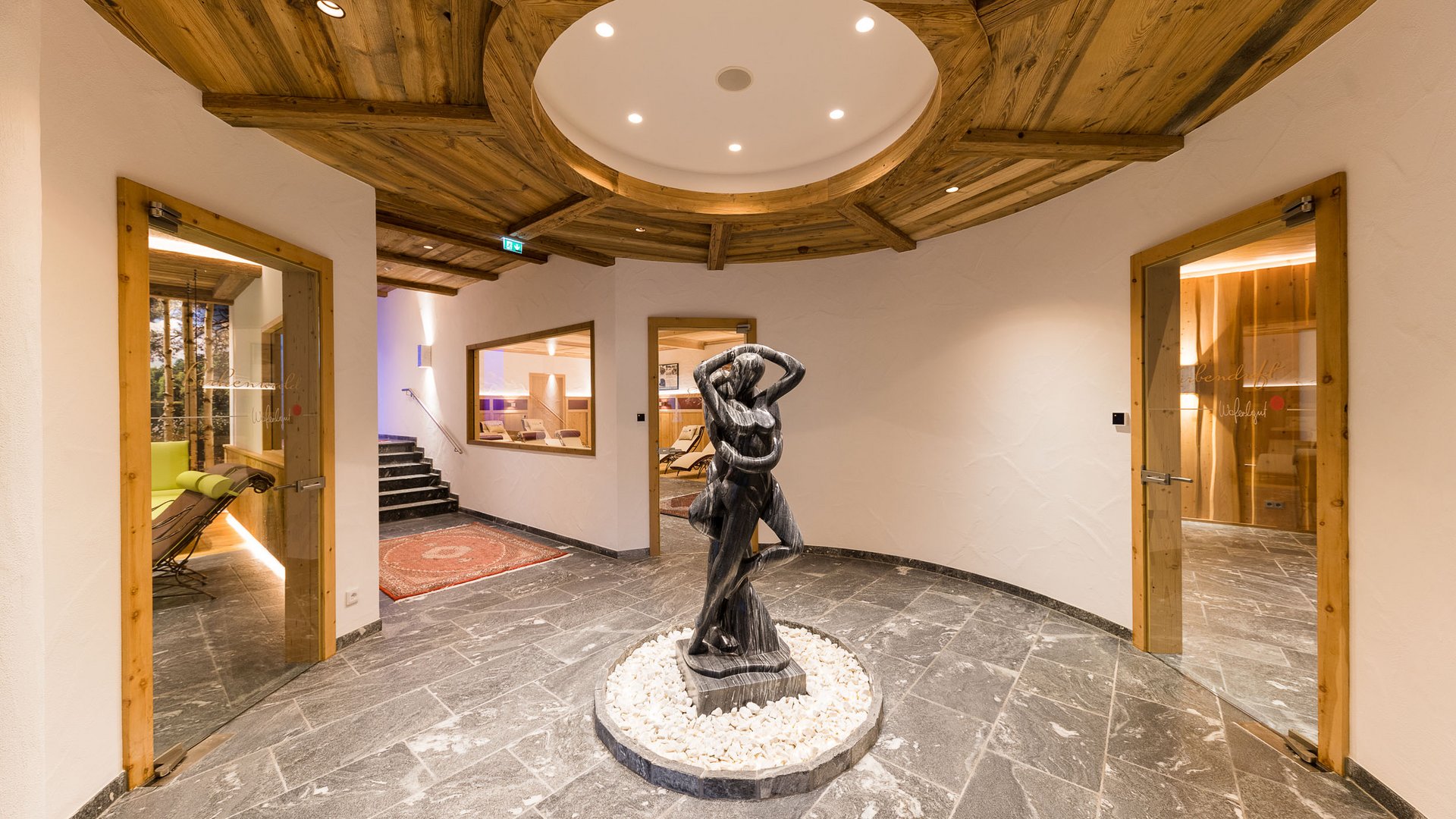 Elegante Lobby mit Skulptur, Naturste**, und rustikaler Holzdecke (© Hotel Woferlgut - Klaus Bauer)